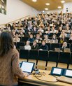 Foto af et fyldt auditorium, hvor en underviser står ved en talerstol med en præsentation foran mange kursusdeltagere på rækker af sæder.