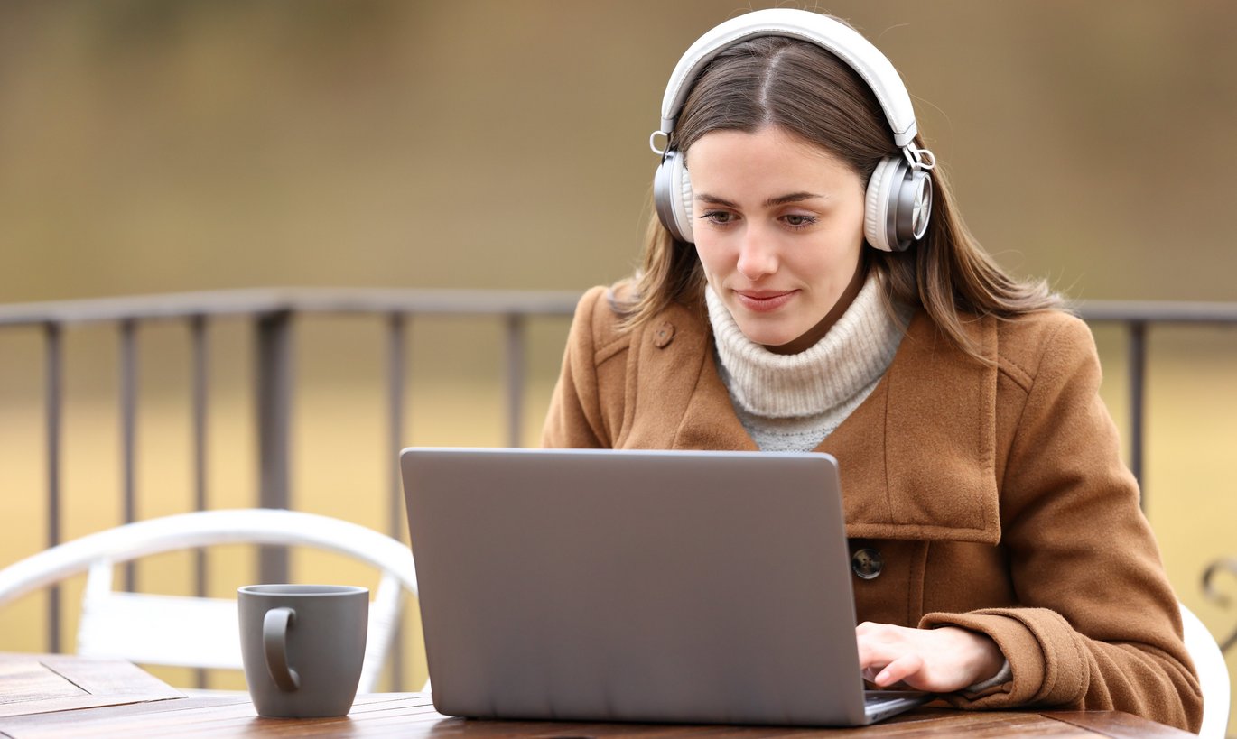 Kvinde med høretelefoner ser medieindhold på en bærbar computer på en terrasse om vinteren